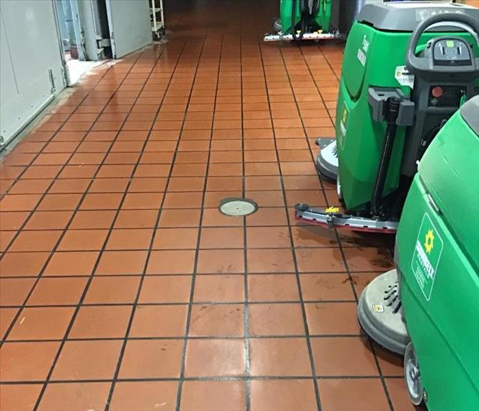Two large green water extractors in a hallway on an orange tile floor.