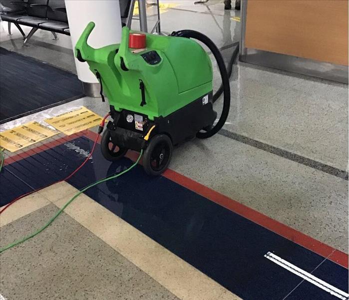 A green water extractor on a tile floor of an office lobby.