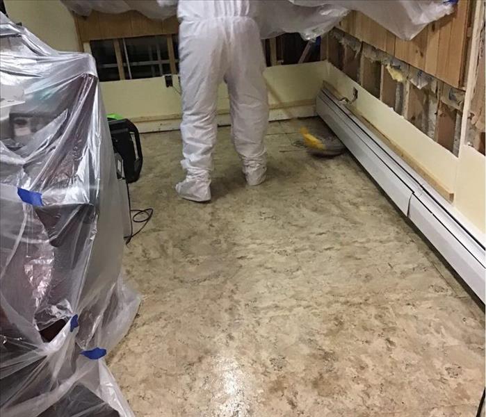 Dirty tile floor with a person in a white suit mopping the floor in the corner.