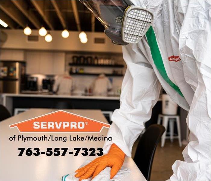 SERVPRO employee wearing PPE and wiping a white table.