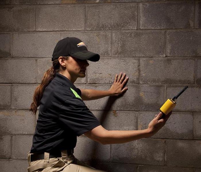 SERVPRO employee holding a yellow water meter in a basement with wet walls.