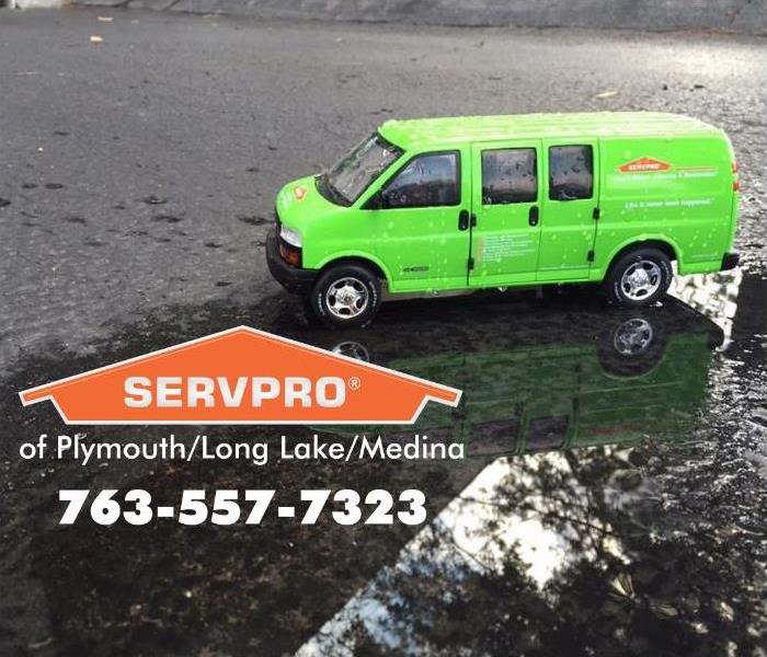 Green van with an orange SERVPRO logo on a black wet street.